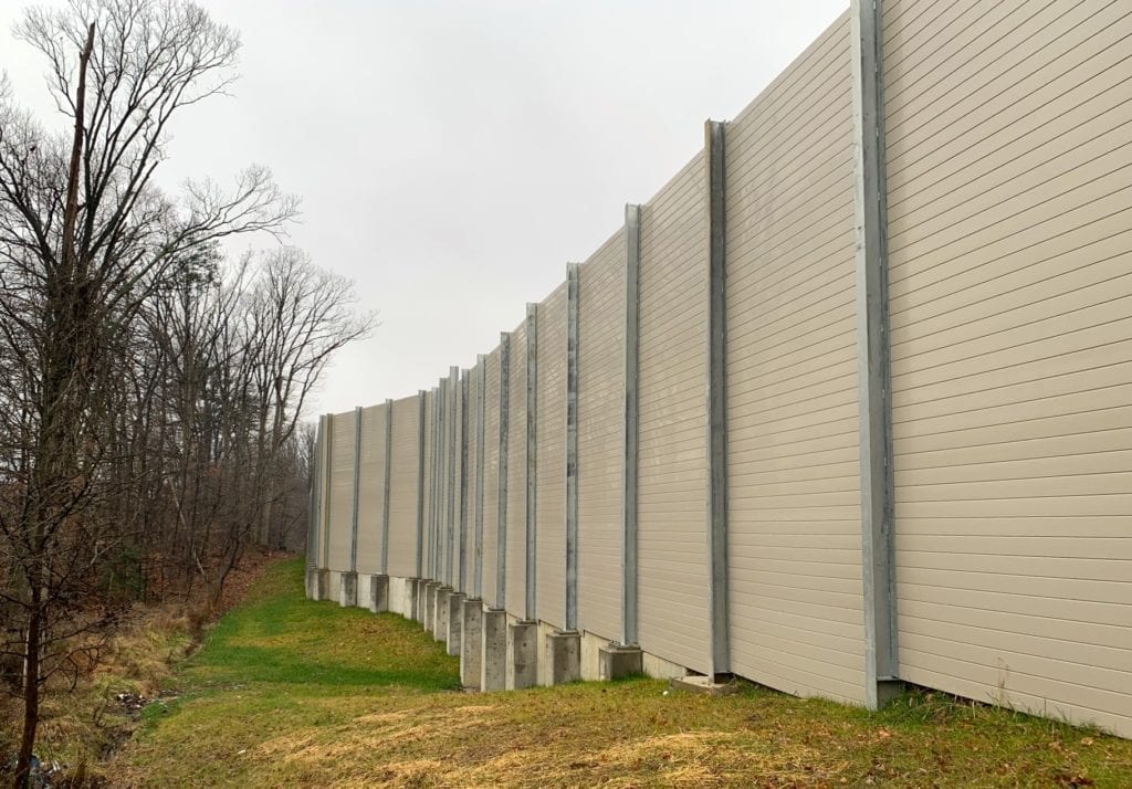 Sound barrier transitions from direct-bury footings to flange-mounted on retaining wall