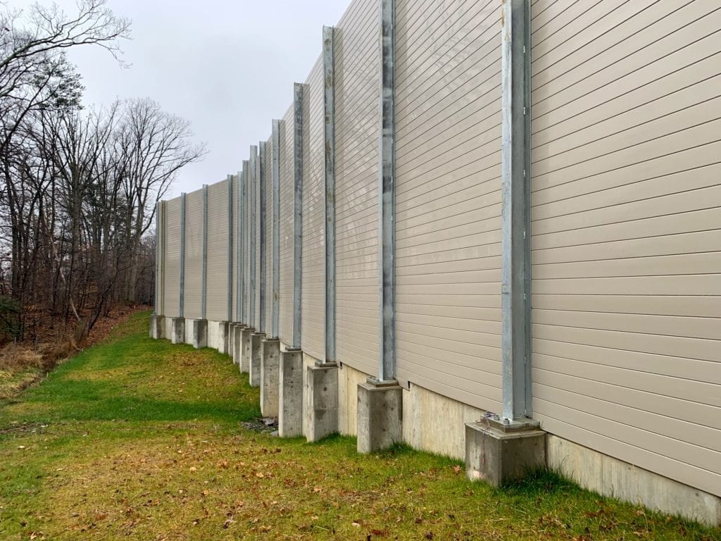 Sound barrier wall flange-mounted to CIP concrete retaining wall