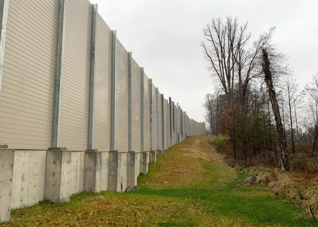 Sound barrier transitions from flange-mounted on retaining wall to direct-bury footings