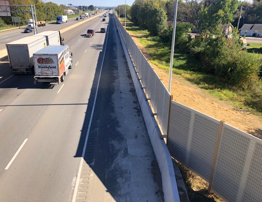 Overpass view of trucks passing highway noise barrier wall